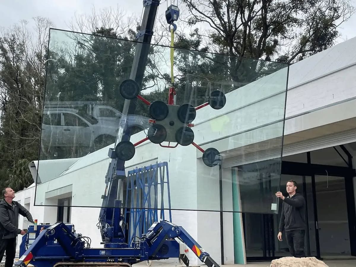 A Man Is Standing Next To A Crane That Is Lifting A Glass Window — South Coast Glass In South Nowra, NSW
