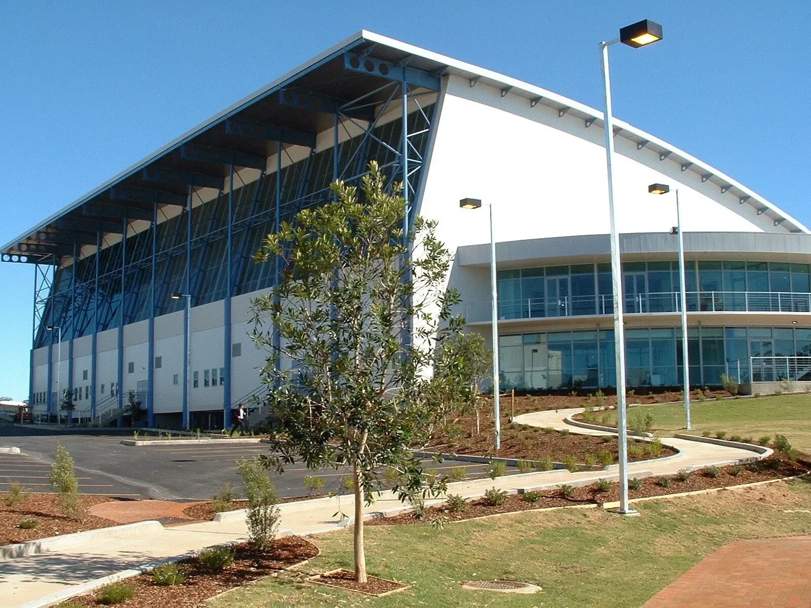 Modern building with curved roof; blue accents, glass windows, landscaping, clear sky — South Coast Glass In South Nowra, NSW