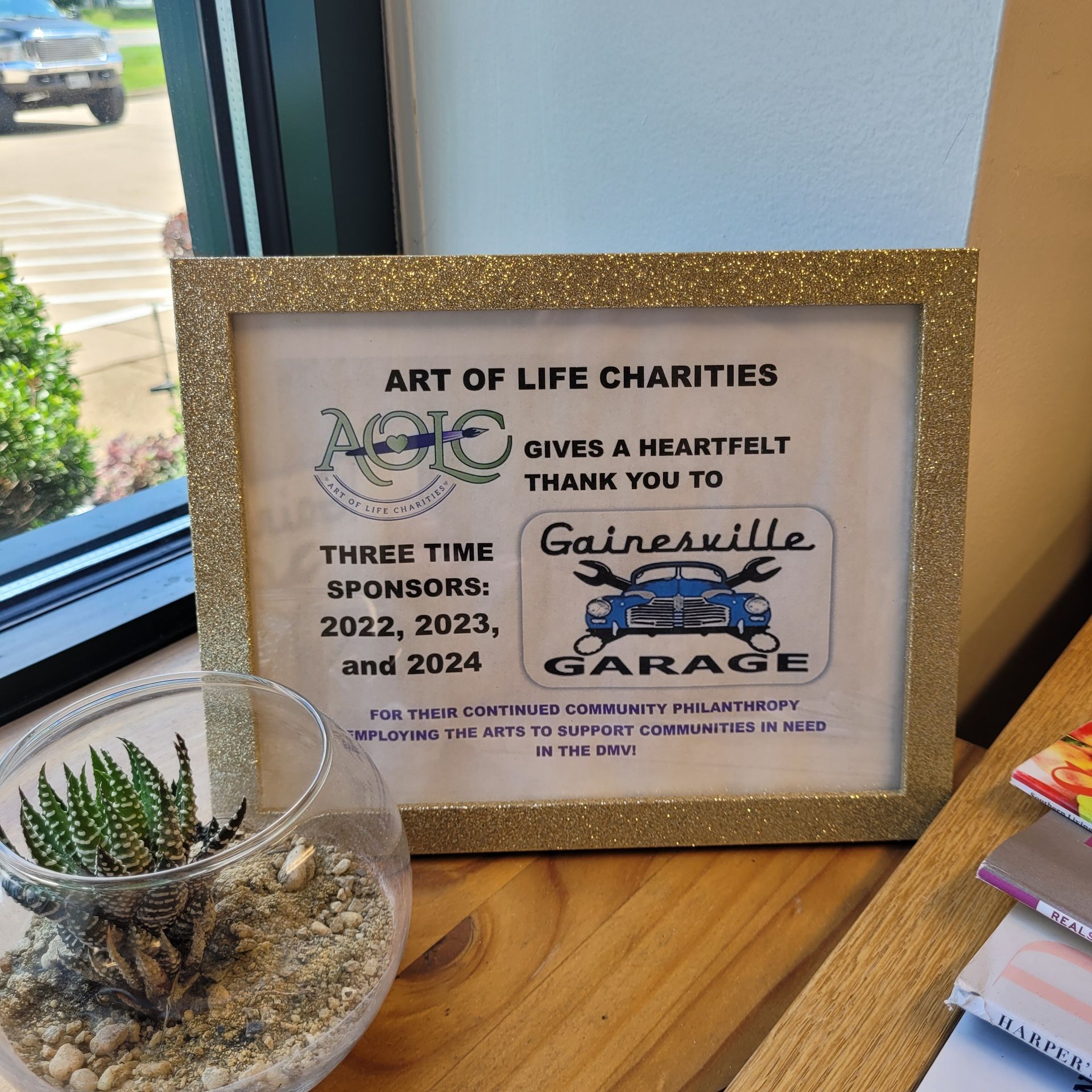 Gold-framed plaque thanking Gainesville Garage from Art of Life Charities. Features logo and sponsor years: 2022, 2023, and 2024. | Gainesville Garage & Trailer Sales