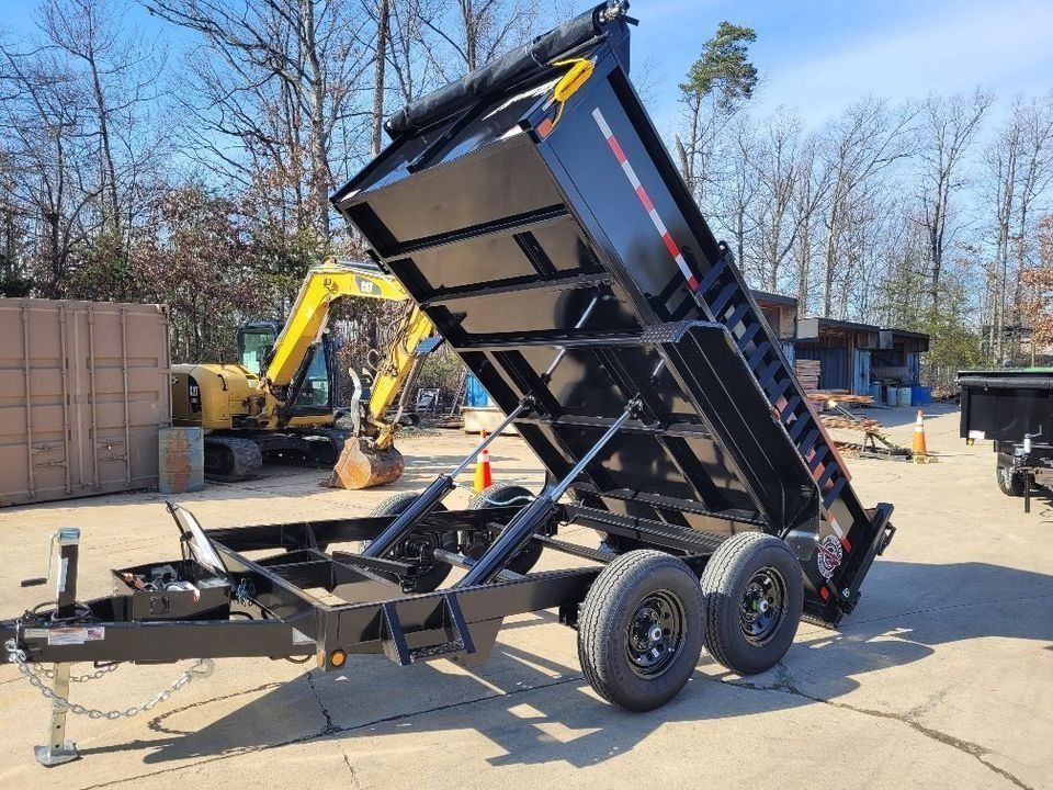 Black dump trailer with raised bed, parked outdoors, with excavator in the background. | Gainesville Garage & Trailer Sales
