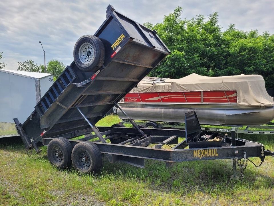 Black dump trailer tilted upwards; two boats visible in the background. | Gainesville Garage & Trailer Sales