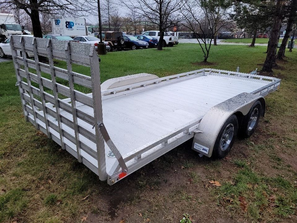 Aluminum utility trailer on grass; two axles, open bed, and a front mesh gate. | Gainesville Garage & Trailer Sales