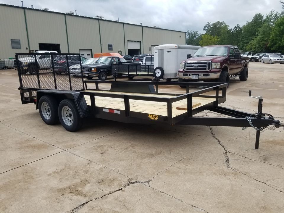 Black utility trailer on a concrete surface, with a truck and other vehicles in the background. | Gainesville Garage & Trailer Sales