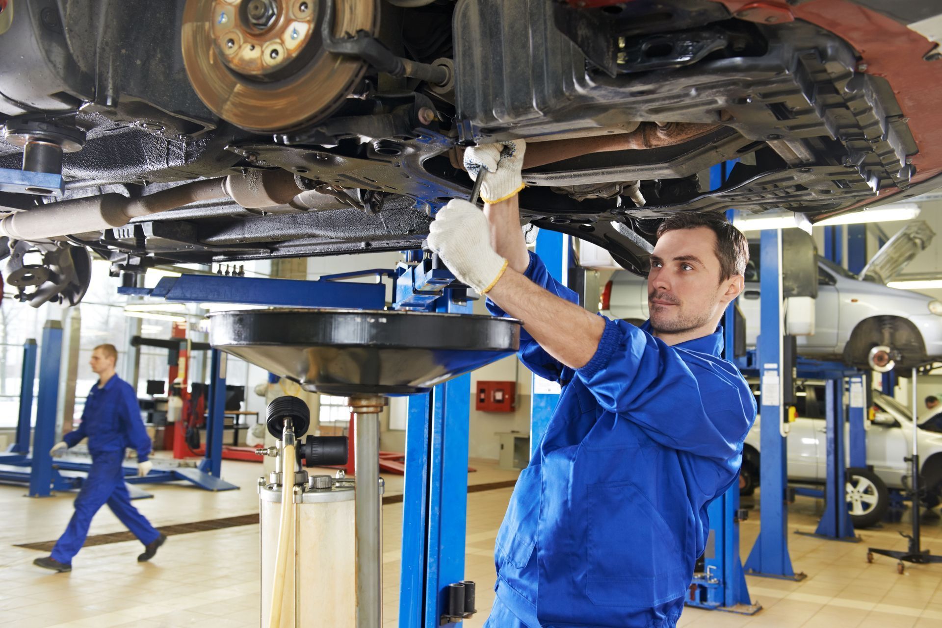 A man is working on the underside of a car in a garage.