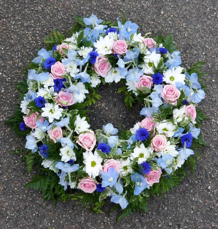 27.  12” traditional white wreath with blue Delphinium’s and Cornflower’s and pink Roses