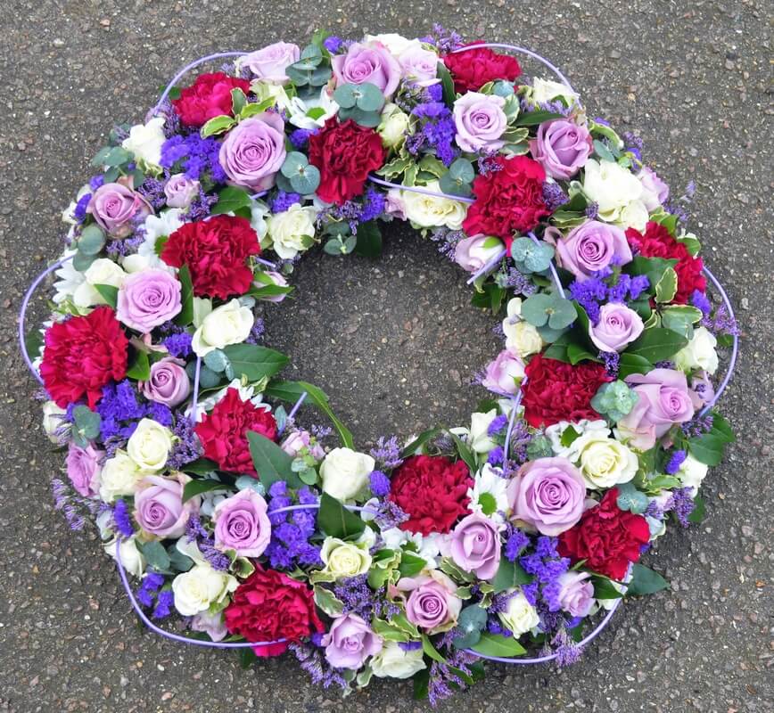 21.  14” traditional wreath colourful purple and white Roses, purple Carnations and Statice