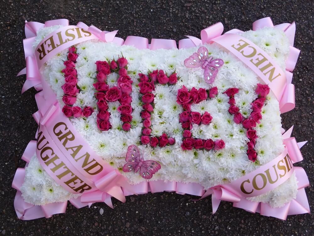 8.  18” white Pillow with pink ribbon edge, sash’s in four corners, name in pink Rosebuds and Butterflies