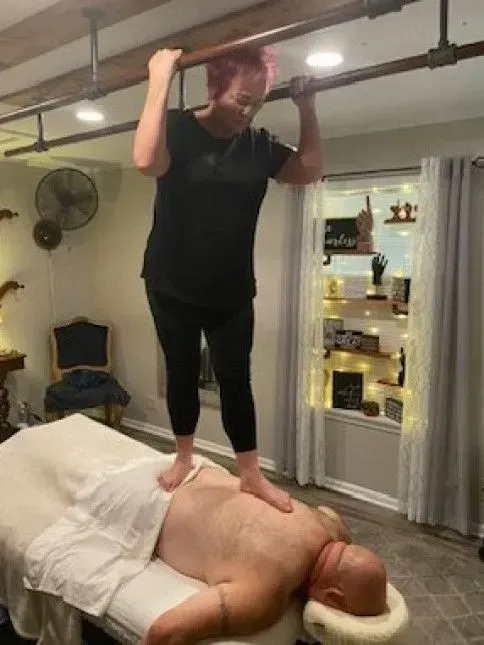 A woman is standing on top of a man laying on a massage table.