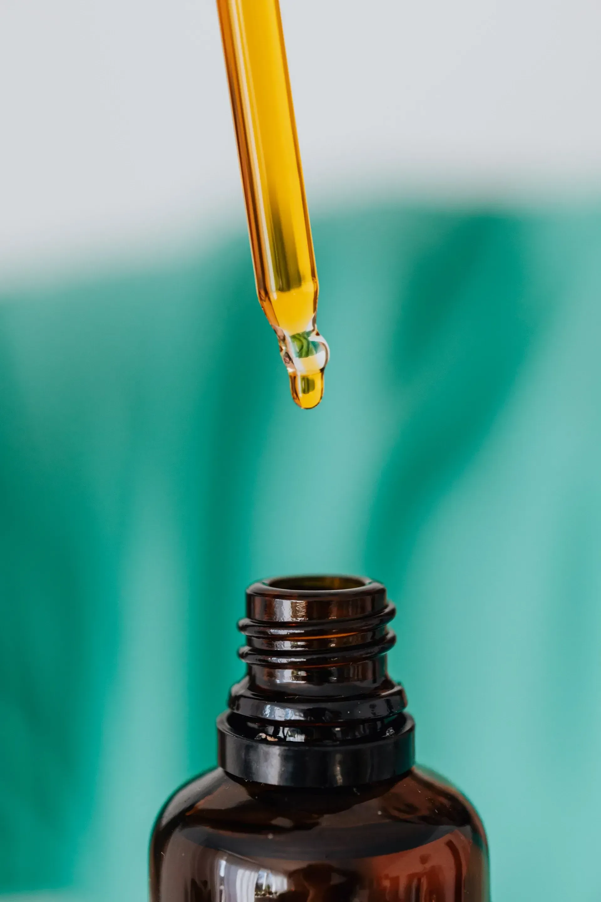 A drop of oil is being poured from a pipette into a bottle.