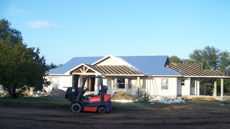Forklift at a house construction site with partially installed blue and brown roofing.