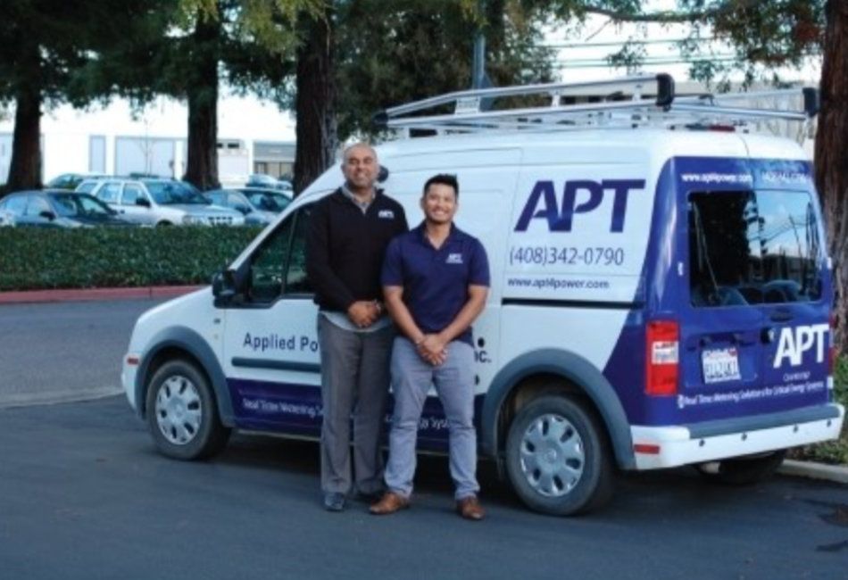 two men standing in front of a van that says ' apt ' on it