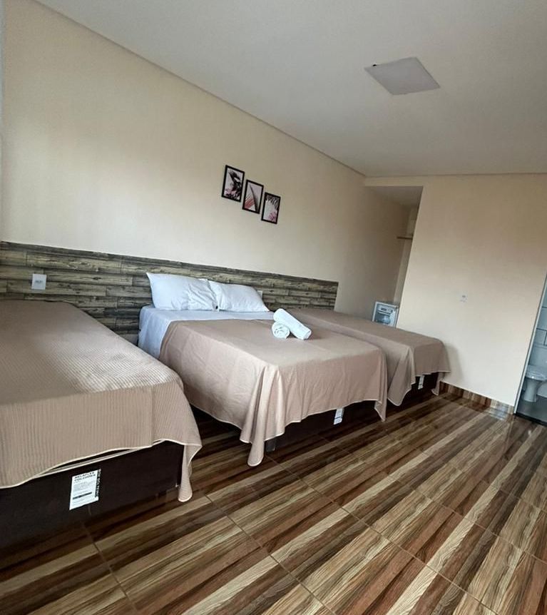 Um quarto de hotel com três camas e piso de madeira.-Pousada-Morada-dos-Passaros