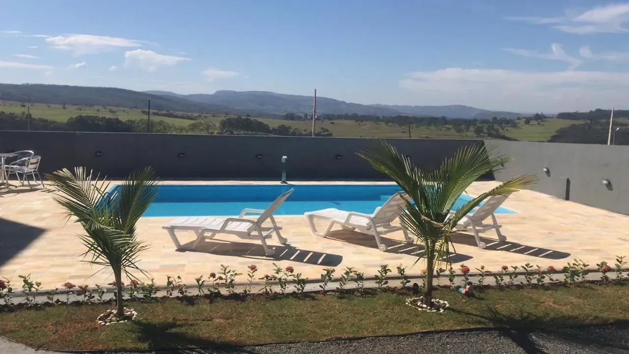 Uma piscina cercada por cadeiras e palmeiras com montanhas ao fundo.-Pousada-Morada-dos-Passaros