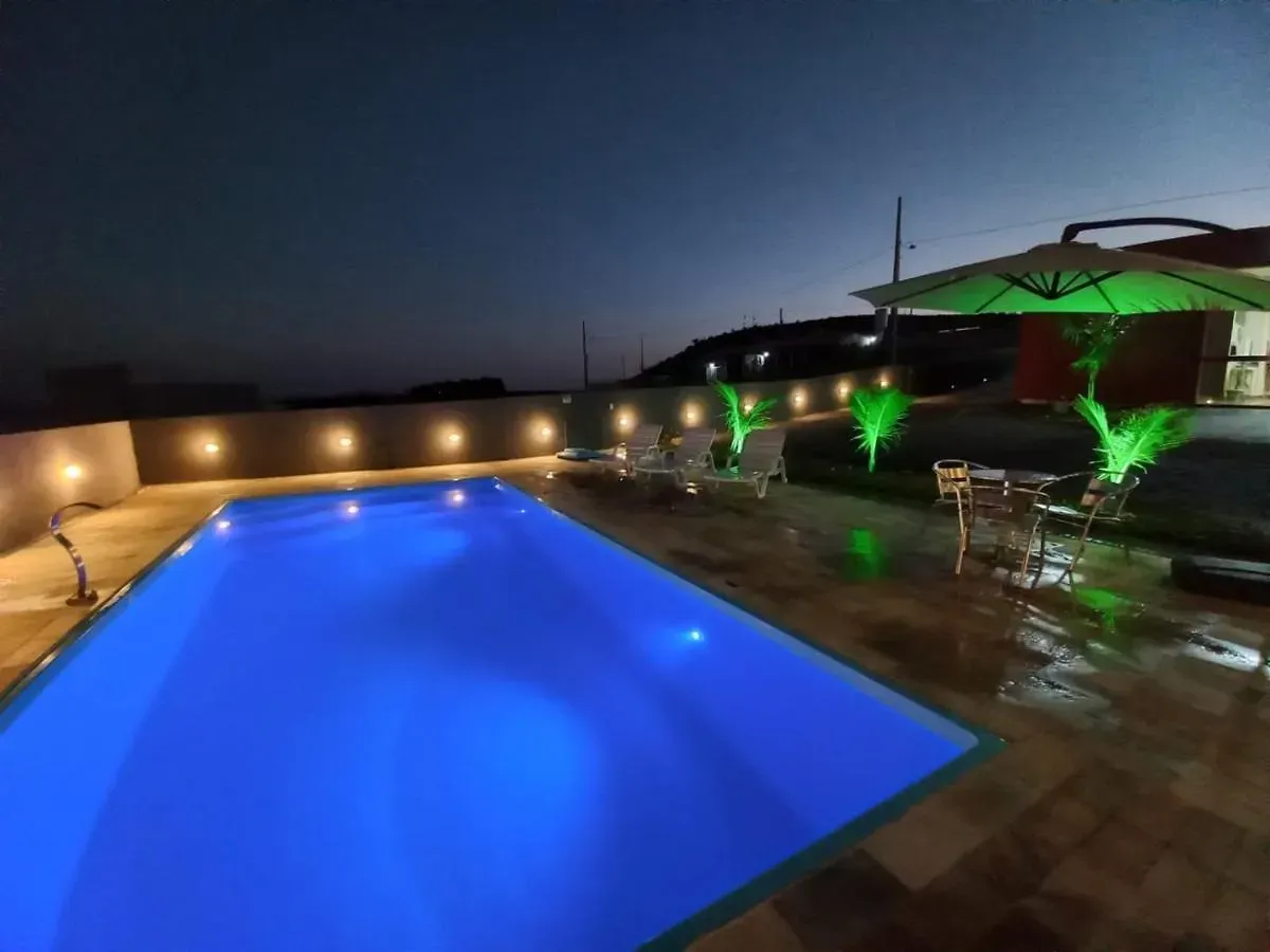 Uma grande piscina é iluminada à noite-Pousada-Morada-dos-Passaros