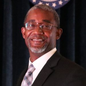 Man in suit and tie, smiling, wearing glasses.
