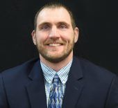 Man smiling in a suit and tie, against a dark background.