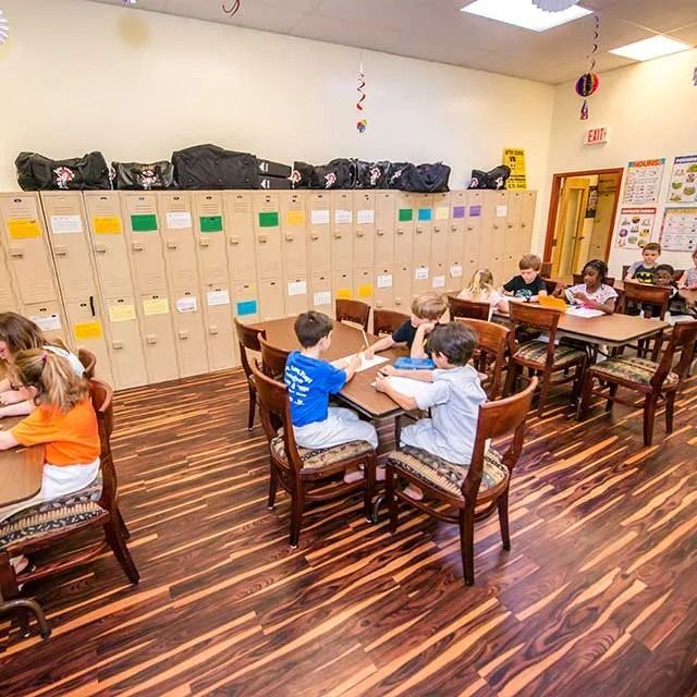 Children seated at tables and desks in a classroom, wood floor, lockers, study.
