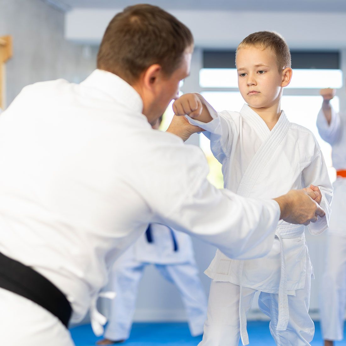 Instructor demonstrating a punch to a young boy in a karate gi; other students in the background.