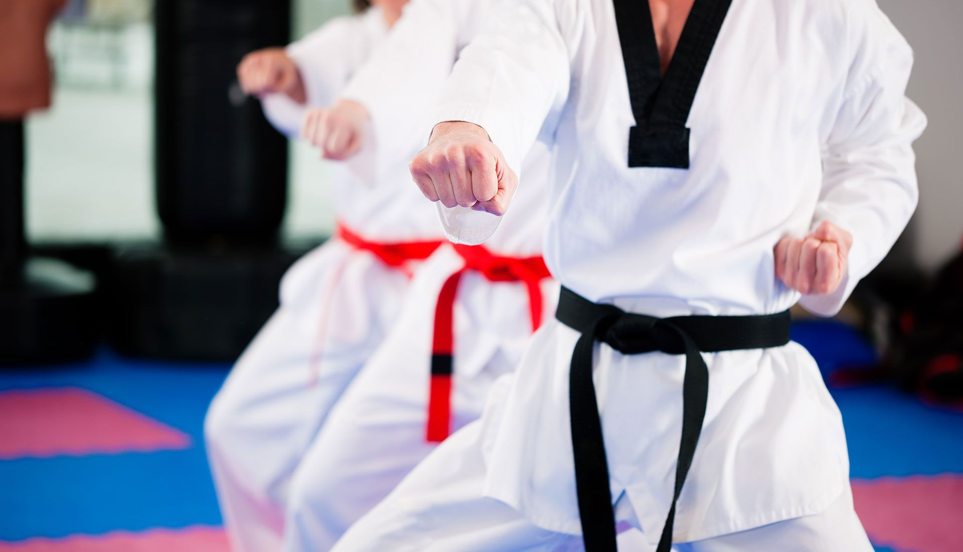 Martial arts practitioners in white uniforms with black and red belts, demonstrating punches.
