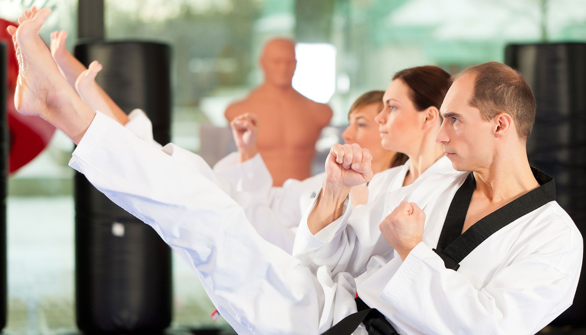 People in karate uniforms practicing kicks in a gym.
