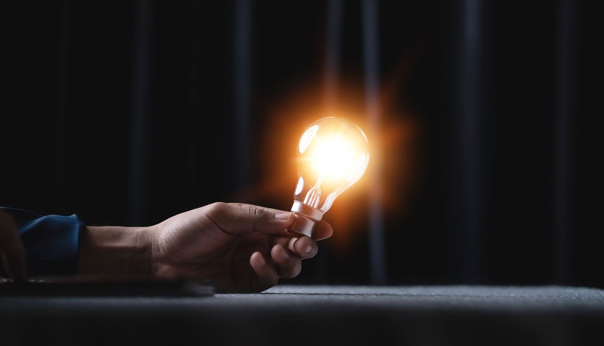 Hand holding a glowing lightbulb in a dark room.
