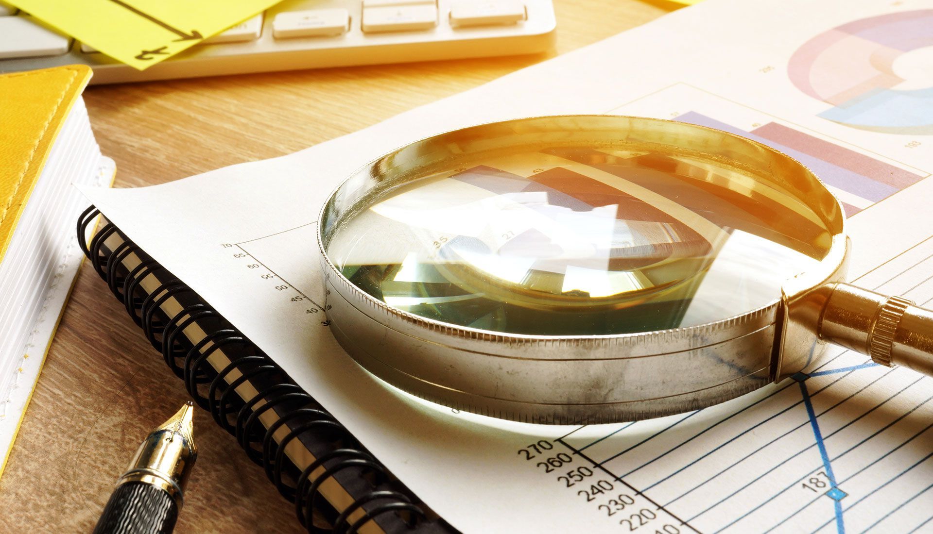 Magnifying glass over documents with graphs and a pen.