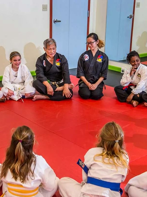 Martial arts class: Students and instructors sit in a circle on a red mat.