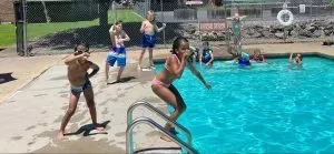 Children near pool, one prepares to jump in. Others are on the side, some in the water.