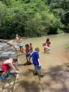 Children playing in a shallow, murky river on a sunny day. 