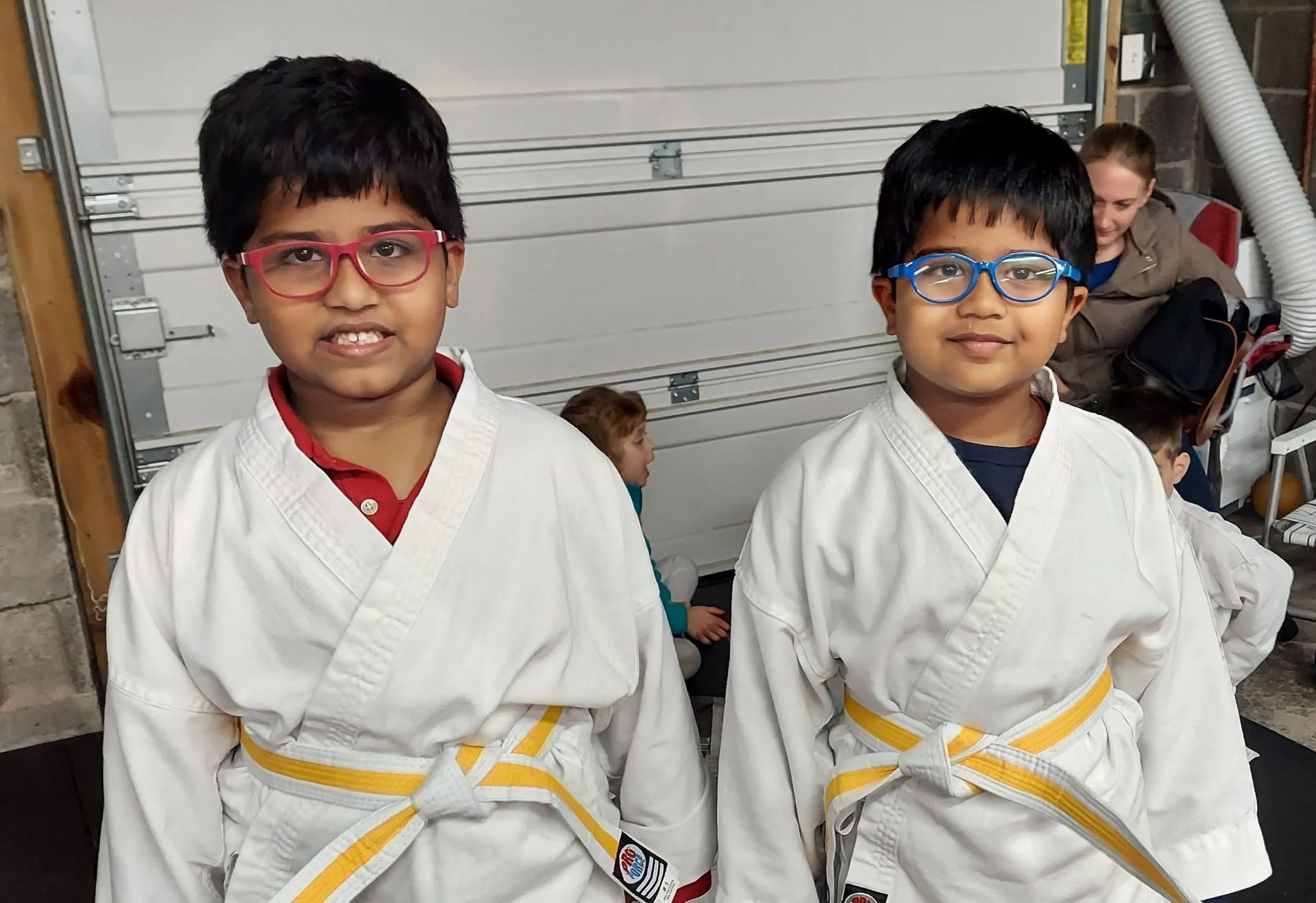 Two children in karate uniforms with yellow belts, smiling.