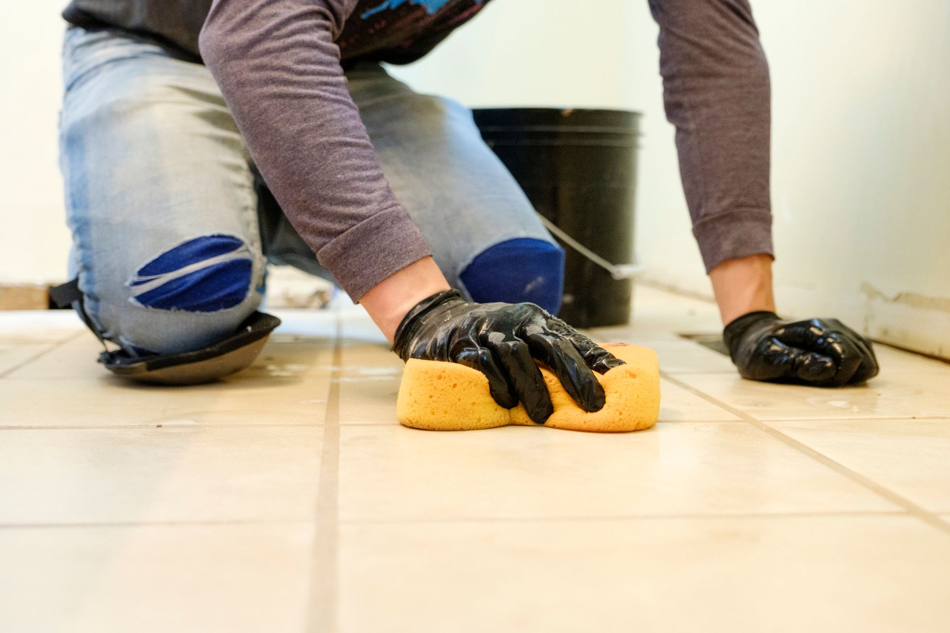 A person is cleaning a tile floor with a sponge.