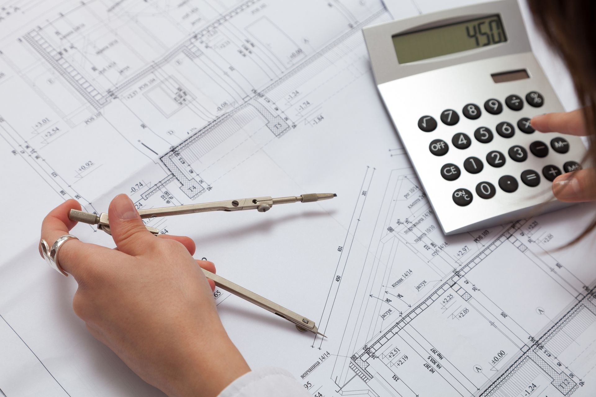 A person using a compass next to a calculator that reads 450