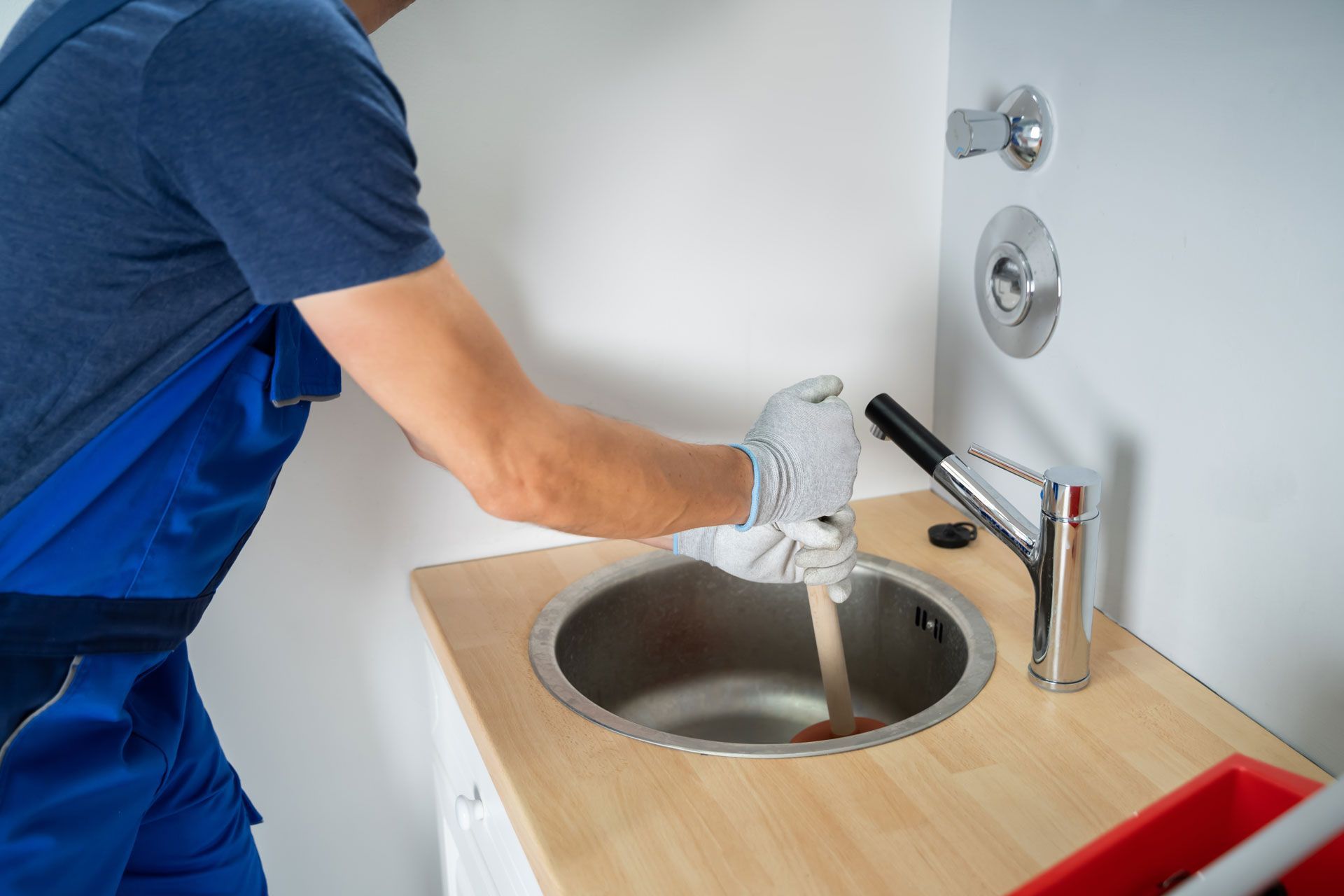 A man is using a plunger to unblock a kitchen sink.