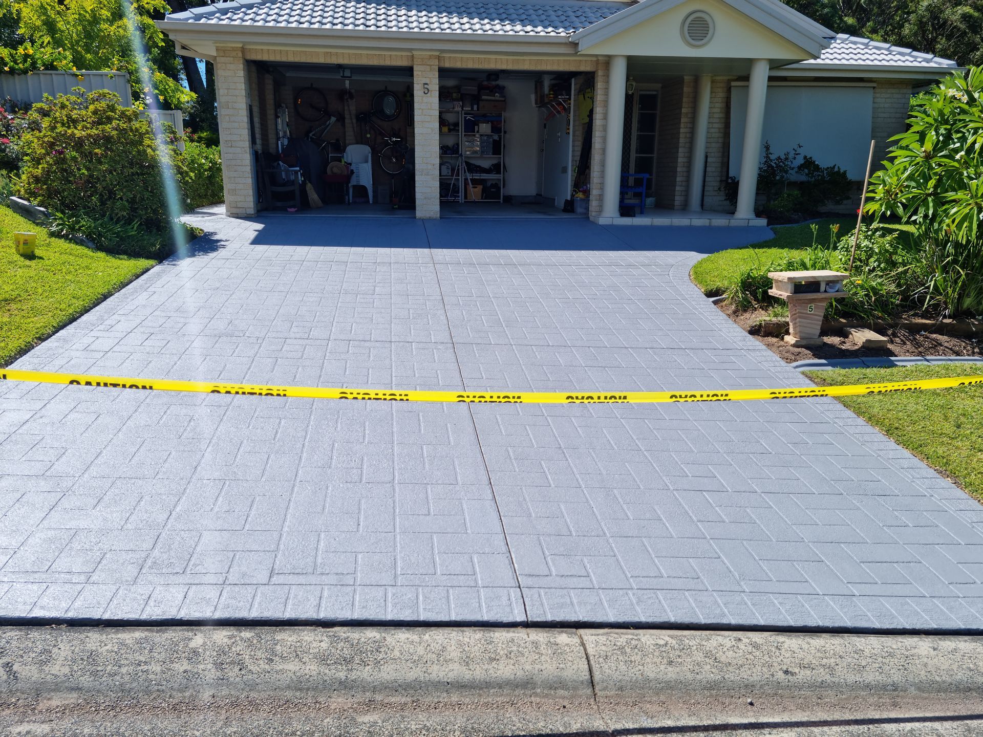 A Gray Driveway With a Yellow Tape on It in Front of a House — All Clean Pressure Cleaning in Valentine, NSW