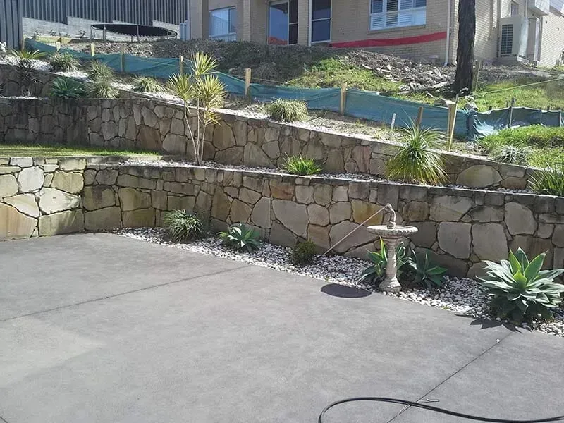 A Concrete Driveway With a Stone Wall in the Background — All Clean Pressure Cleaning in Valentine, NSW
