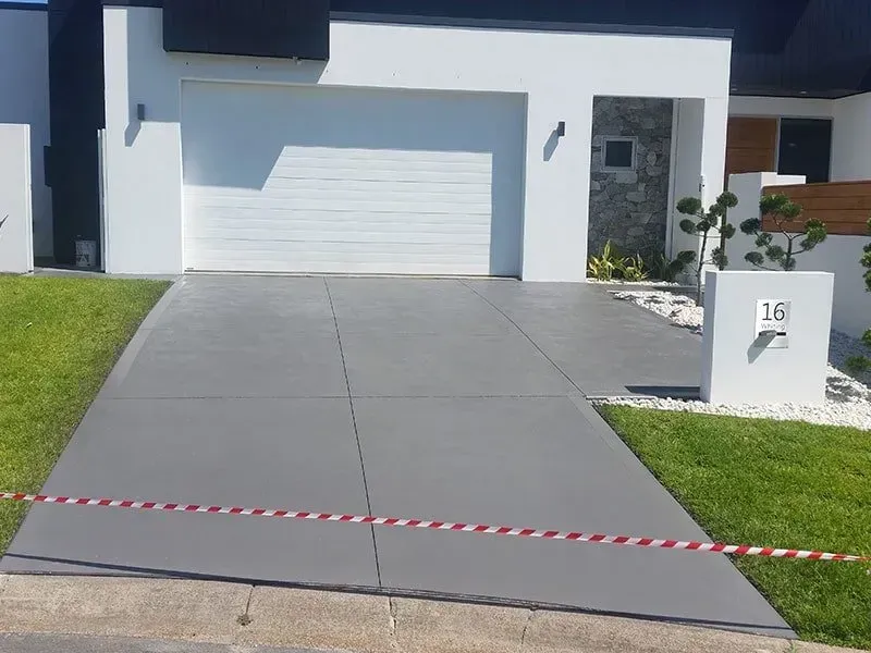 A Concrete Driveway Leading to a House With a White Garage Door — All Clean Pressure Cleaning in Valentine, NSW
