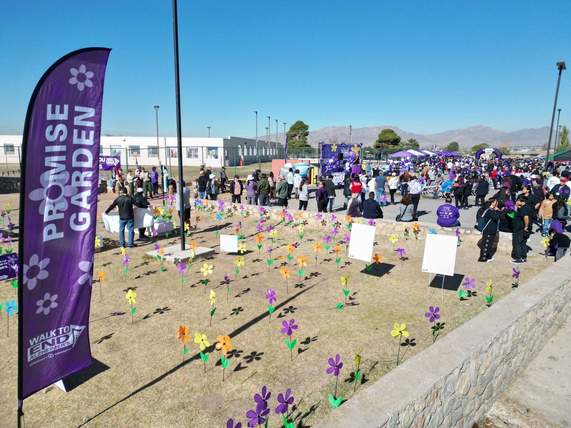 A large group of people are gathered in a field with flowers and a banner that says promise garden.