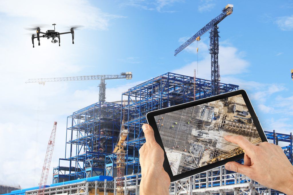 Construction site with DJI drone, cranes, workers in safety gear, and a tablet showing aerial view for safety monitoring.