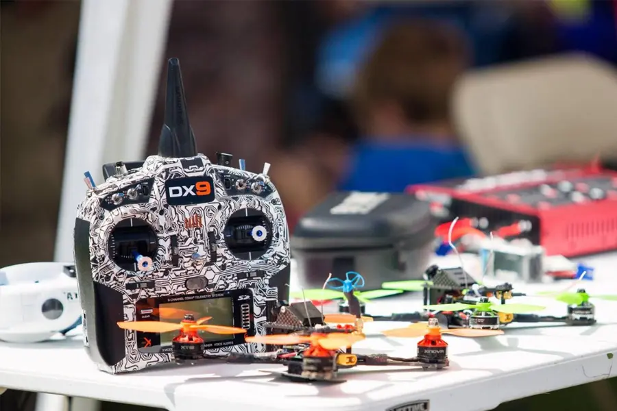 Drone remote controller with a battery indicator on a worktable, next to a modern drone, surrounded by repair tools in a professional workshop setting.