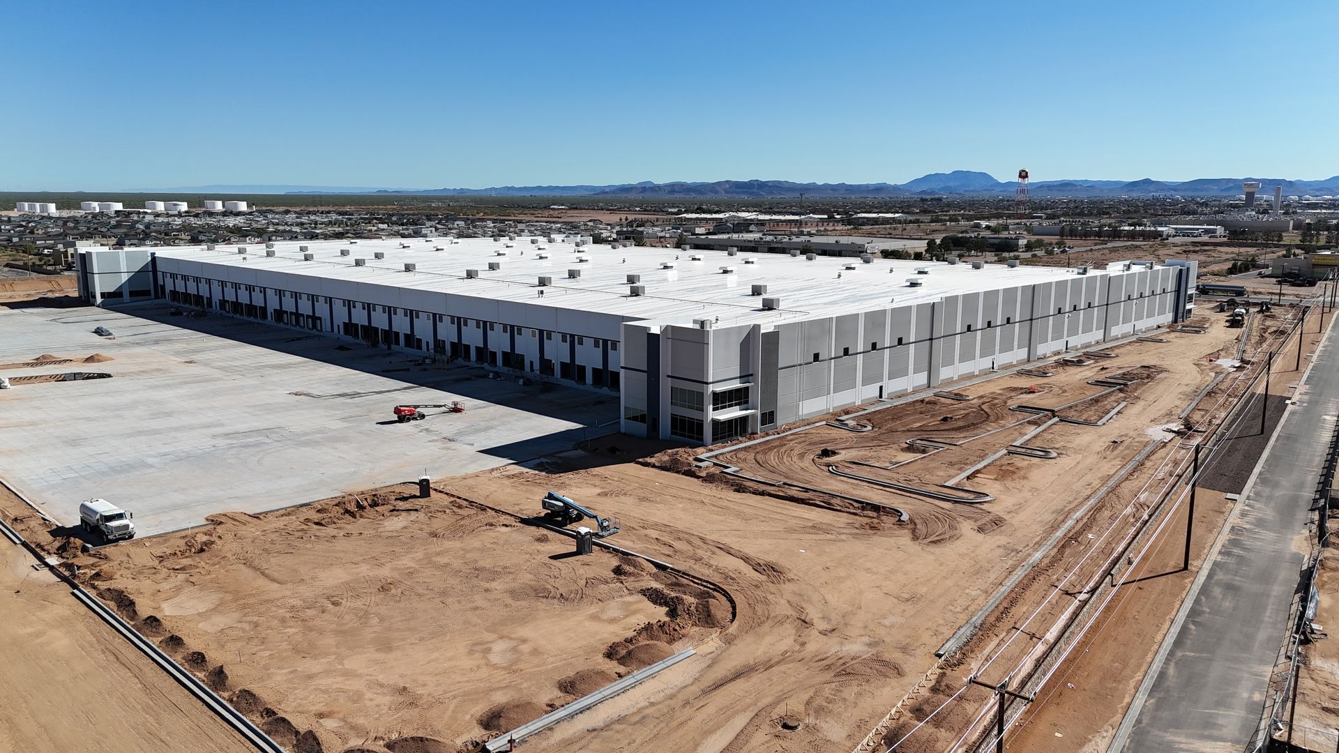 Aerial drone view of a large industrial warehouse under construction in El Paso, Texas with surrounding desert landscape.