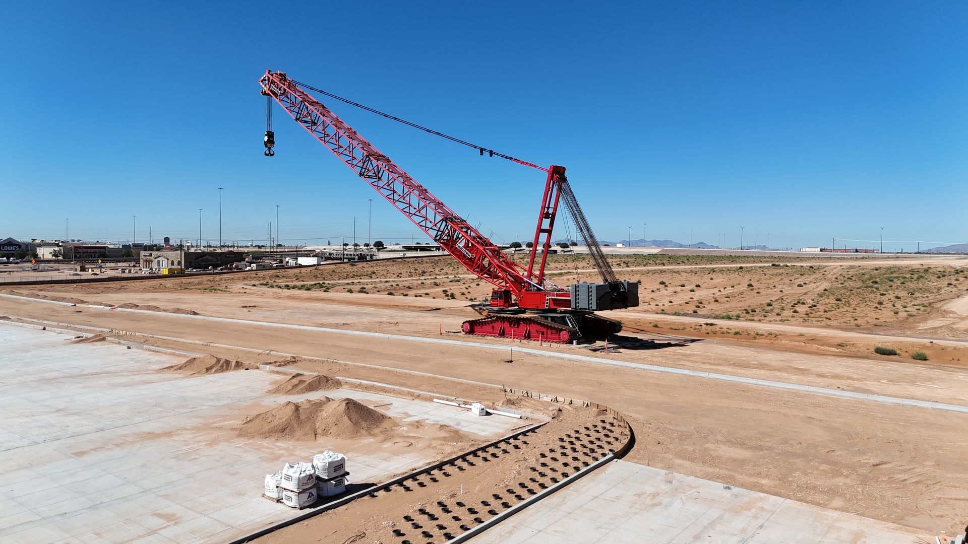 A red crawler crane extends across the frame as part of the construction of a new warehouse facility.