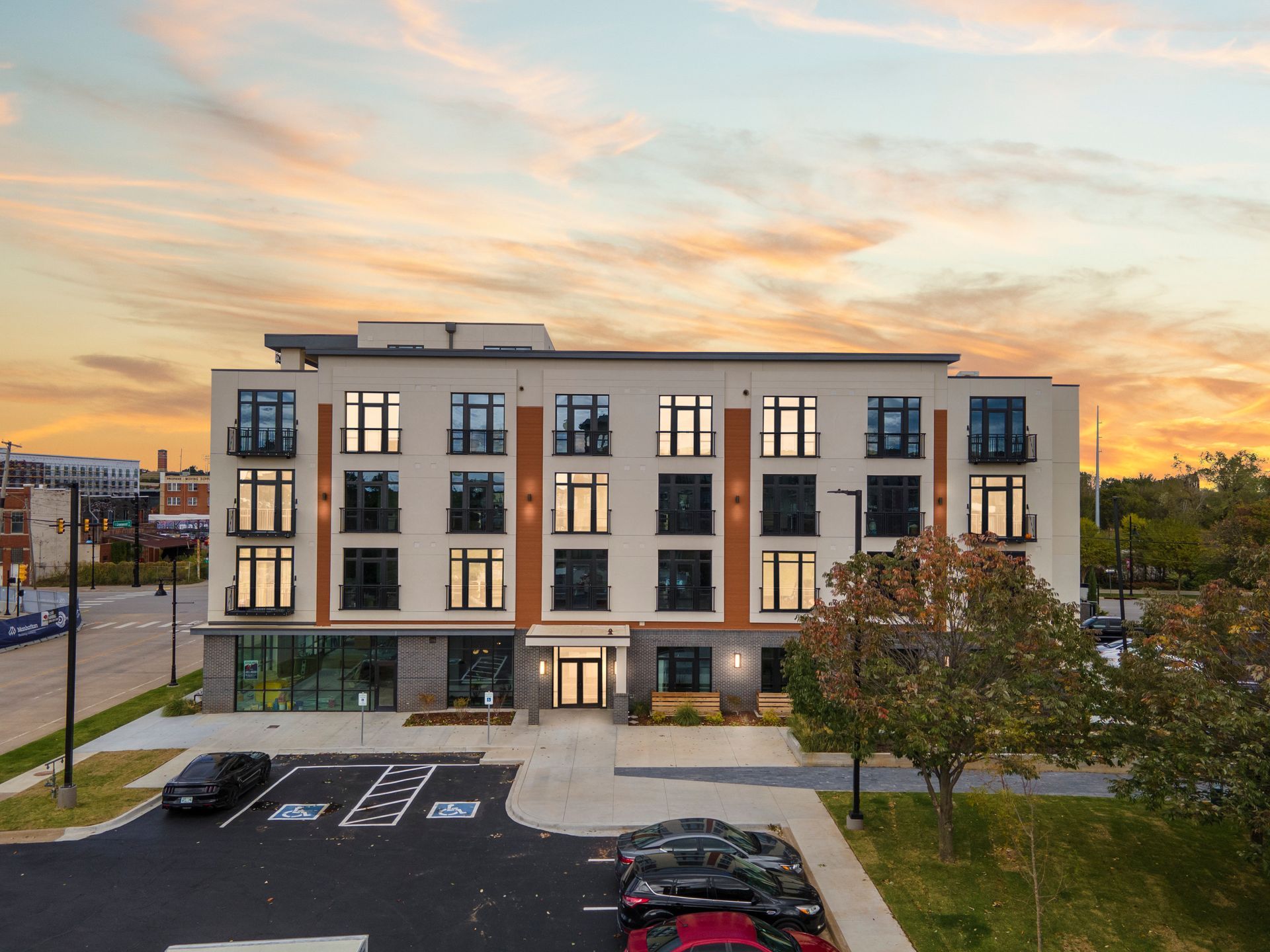 Modern multi-story building at sunset, with cars parked in front.