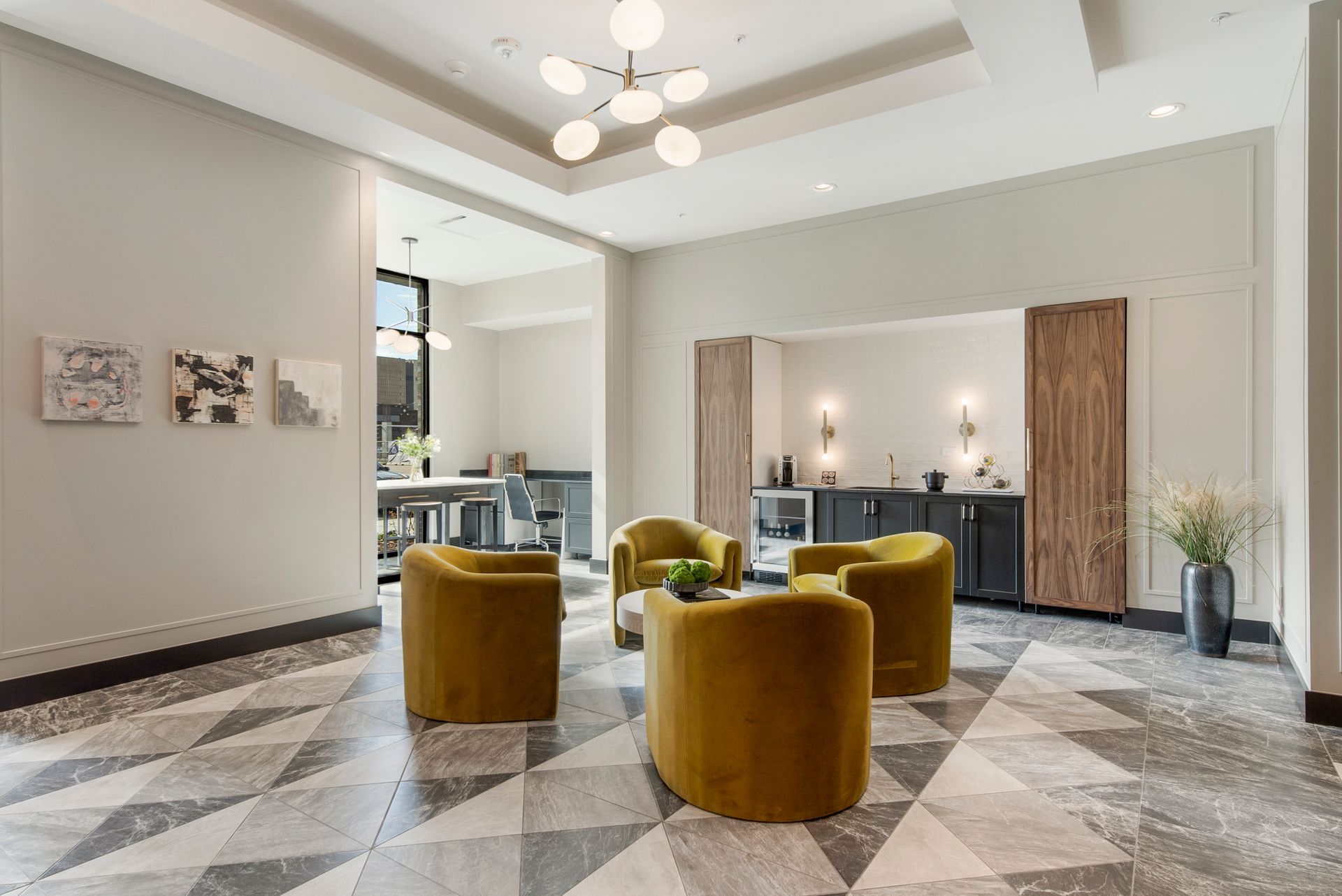Lounge area with four gold armchairs, gray and white geometric floor, and a small kitchenette.