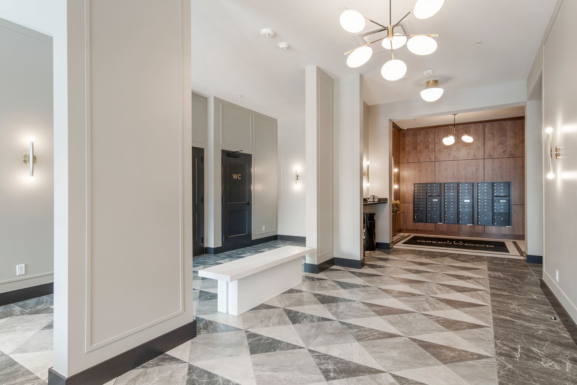 Hallway with geometric floor, columns, mailboxes, and modern lighting.