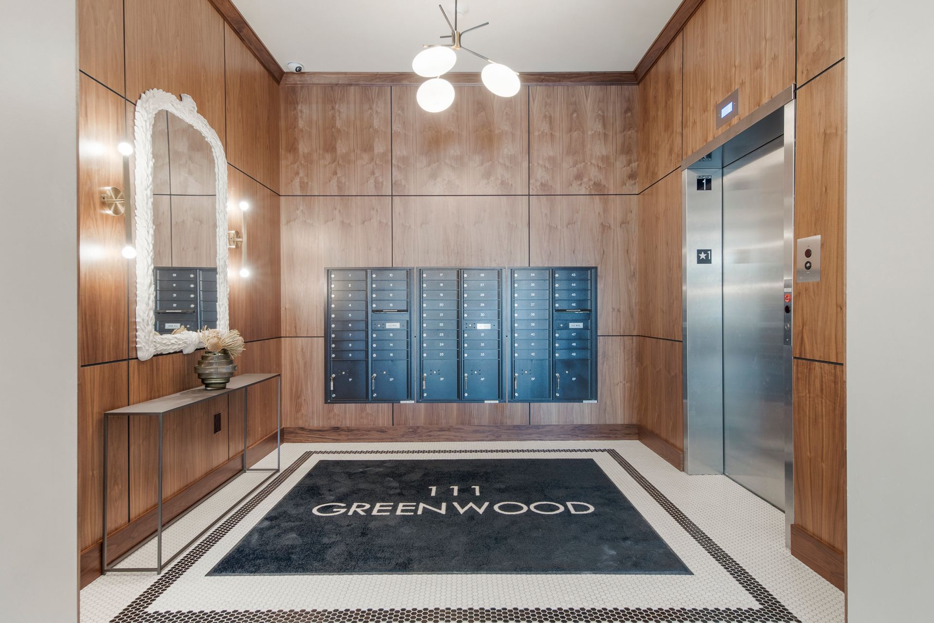 Apartment lobby with wood paneling, mailboxes, elevator, mosaic tile floor, and mirror.
