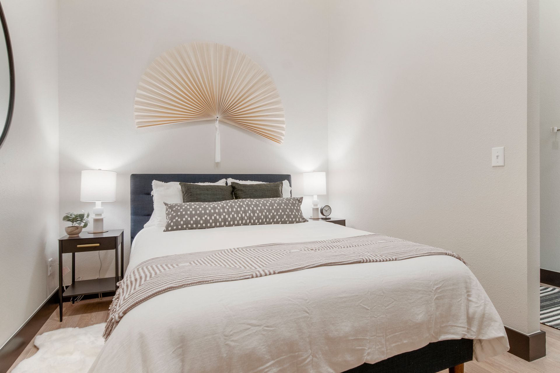 Bedroom with white walls, bed with pillows, nightstands, and gold fan decor.