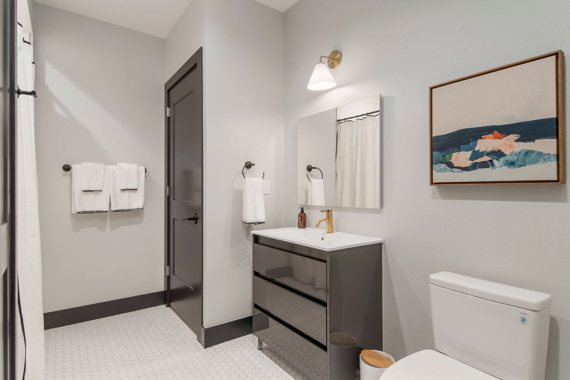 Bathroom with gray walls, white sink and toilet, and artwork.