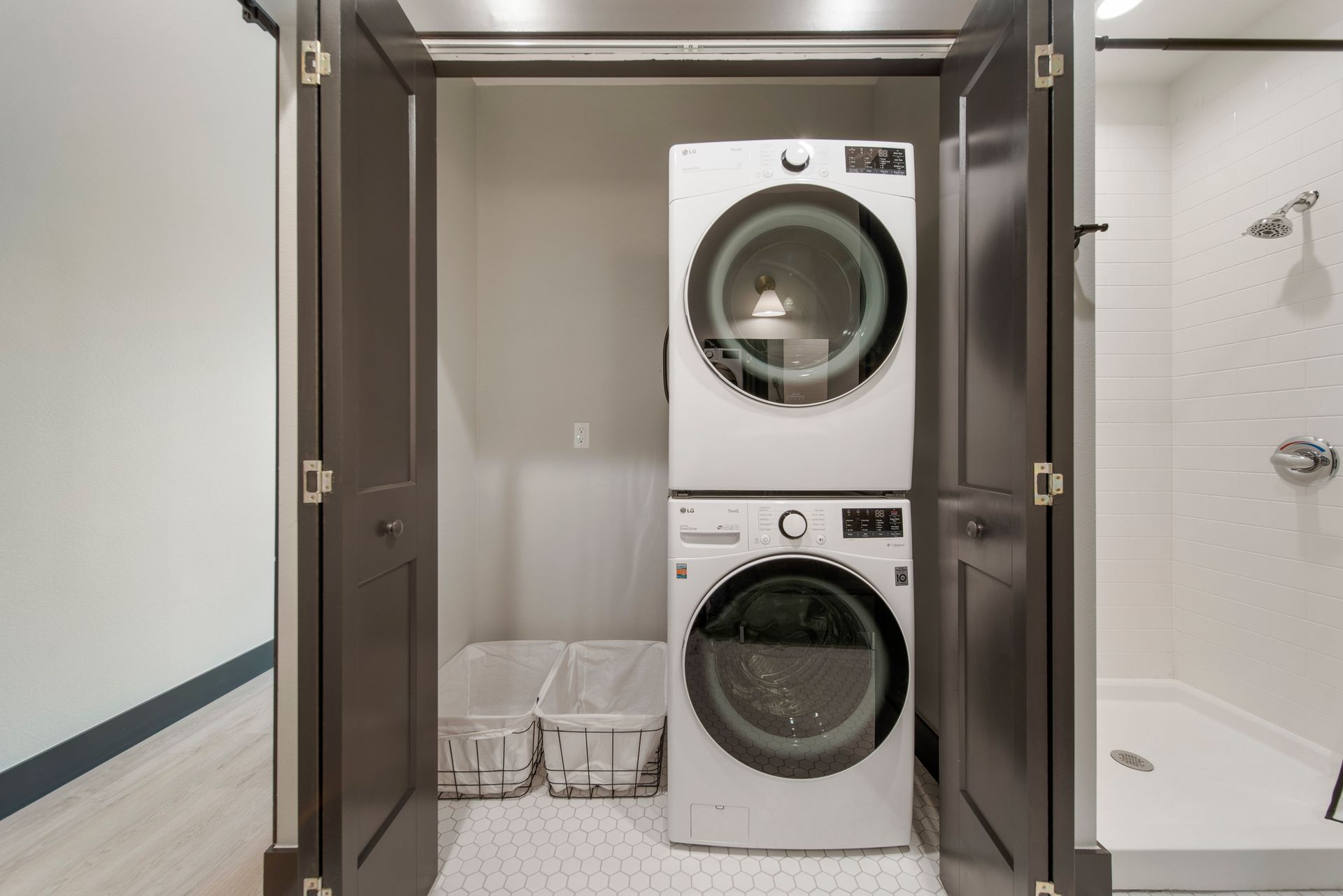 Stacked washer and dryer in a closet with open brown doors, next to a shower.