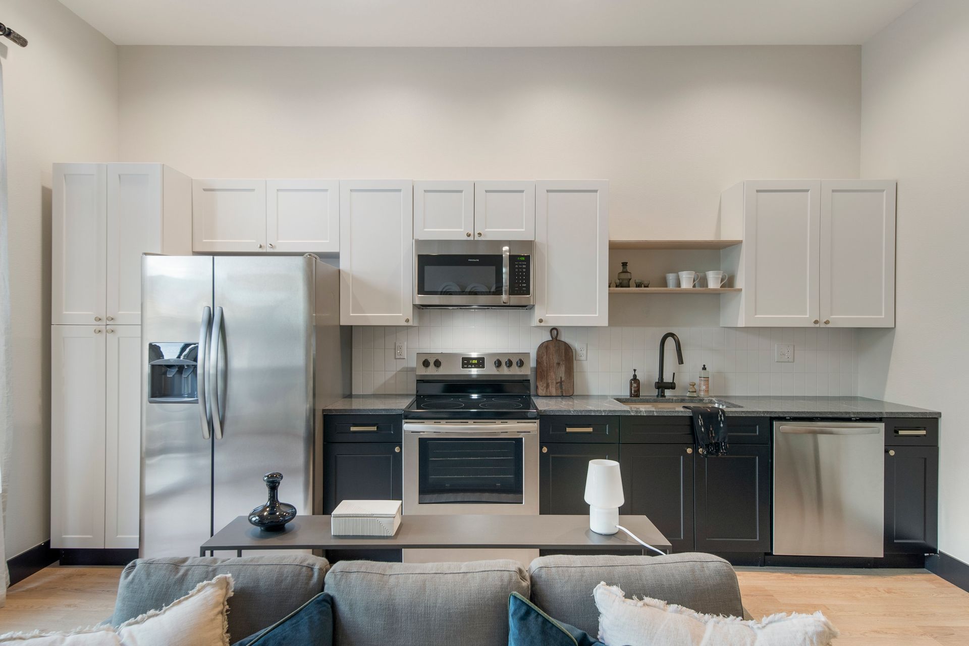 Modern kitchen with stainless steel appliances, white and black cabinets, and a gray sofa in front.