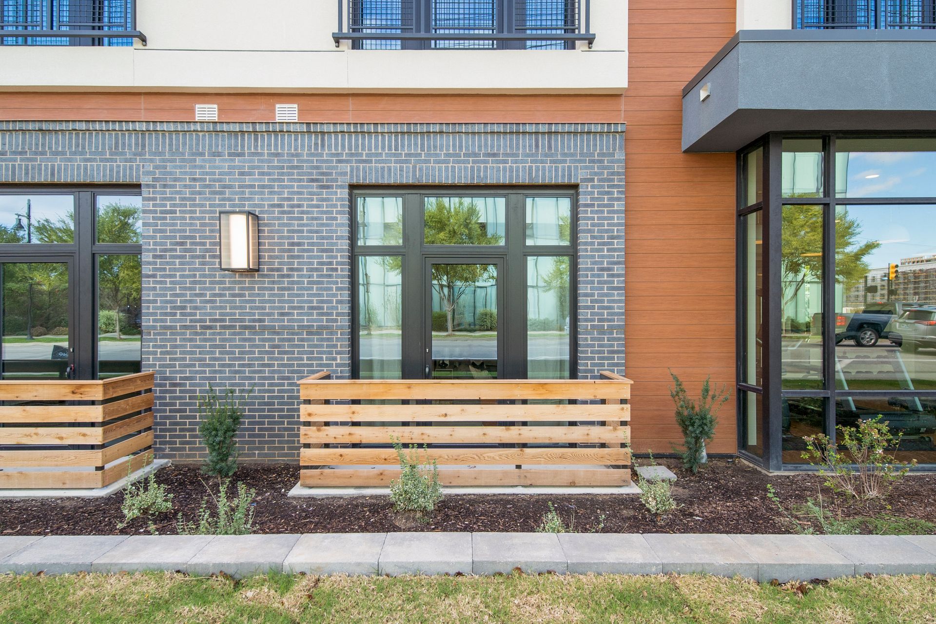 Exterior of a modern building with dark-framed windows, brick, and wooden planters.